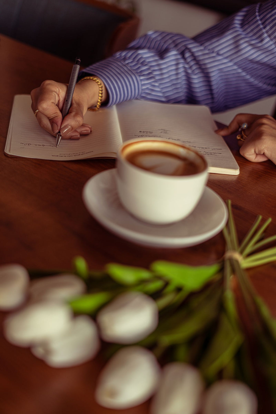 Woman writing in a journal beside coffee and tulips