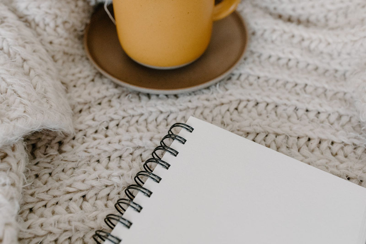 Blank notebook and mug on a knitted blanket