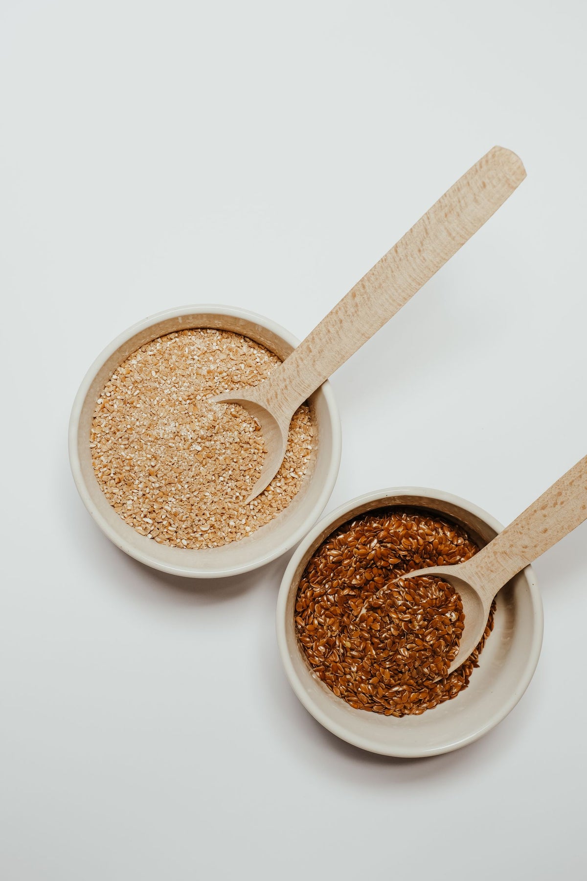 Flax and oats in ceramic bowls with wooden spoons