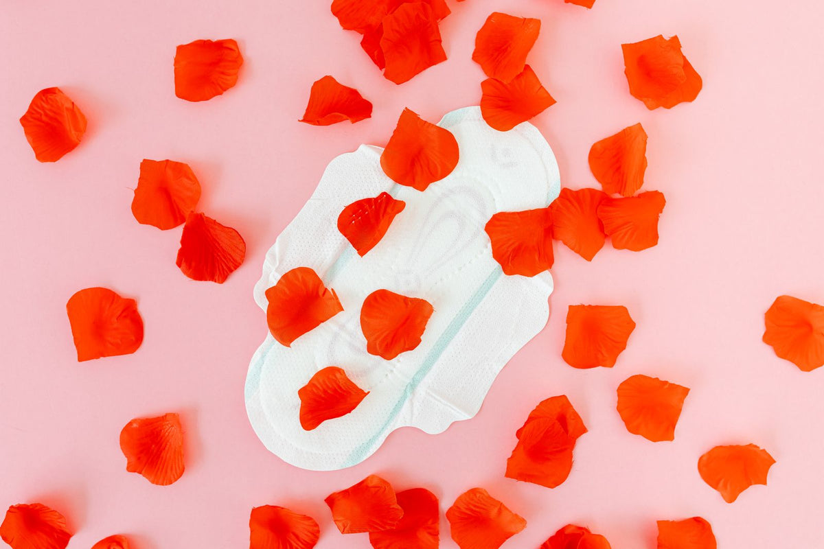 Sanitary pad surrounded by red petals on a pink background