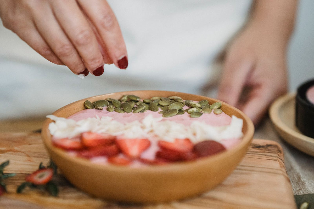 Hand topping a smoothie bowl with seeds and strawberries