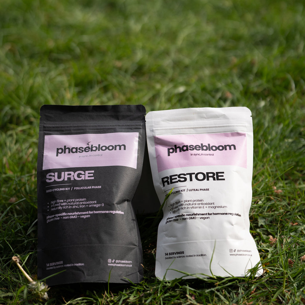 Two Phasebloom seed cycling kit product packages, 'Surge' and 'Restore', on grass.