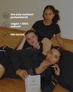 Three women in black clothing pose on a wooden floor indoors, with text overlays highlighting product benefits: 'the only nutrient-protected kit,' 'vegan + 100% natural,' and 'lab tested.' One woman holds a white product box labeled phasebloom seed cycling kit